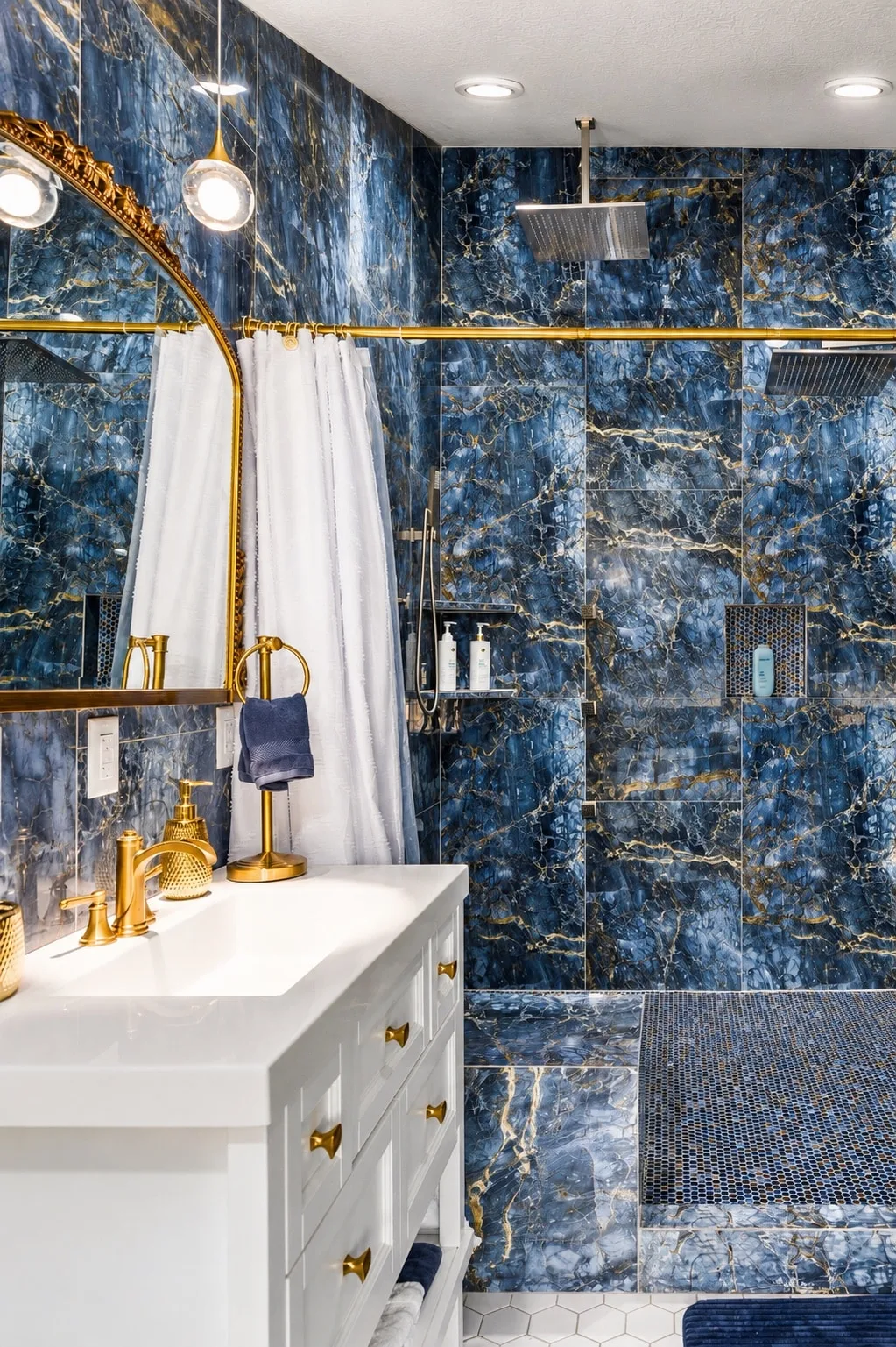Sky Suite ensuite: matching blue-and-gold marble walk-in shower with dual rainfall shower heads, arched gold mirror, and a mosaic-tile shower floor.