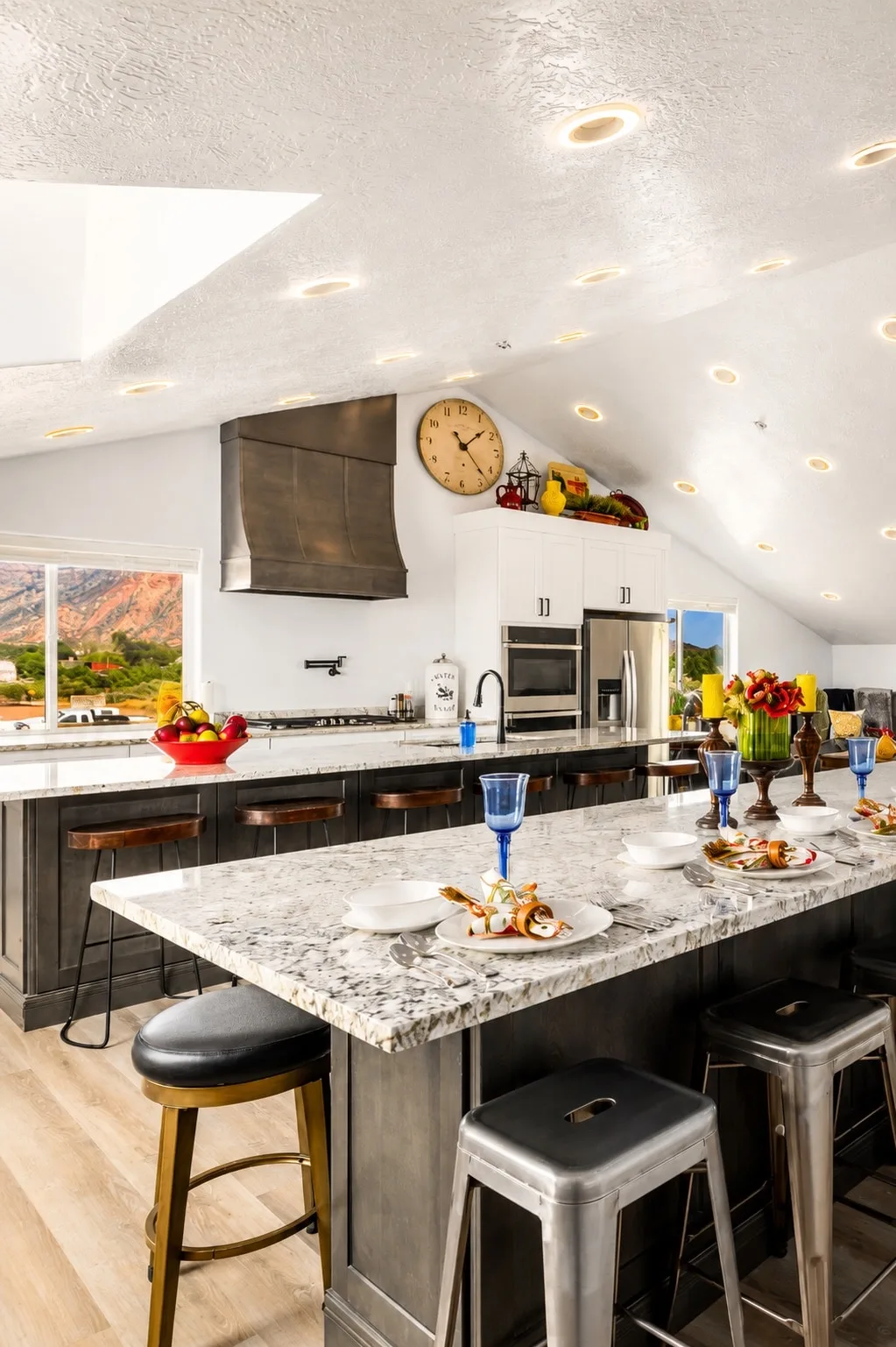 Sky Suite's vaulted great-room kitchen: dark-base granite island seating six, skylit ceiling, Spanish-style range hood, and red-rock views out the window.