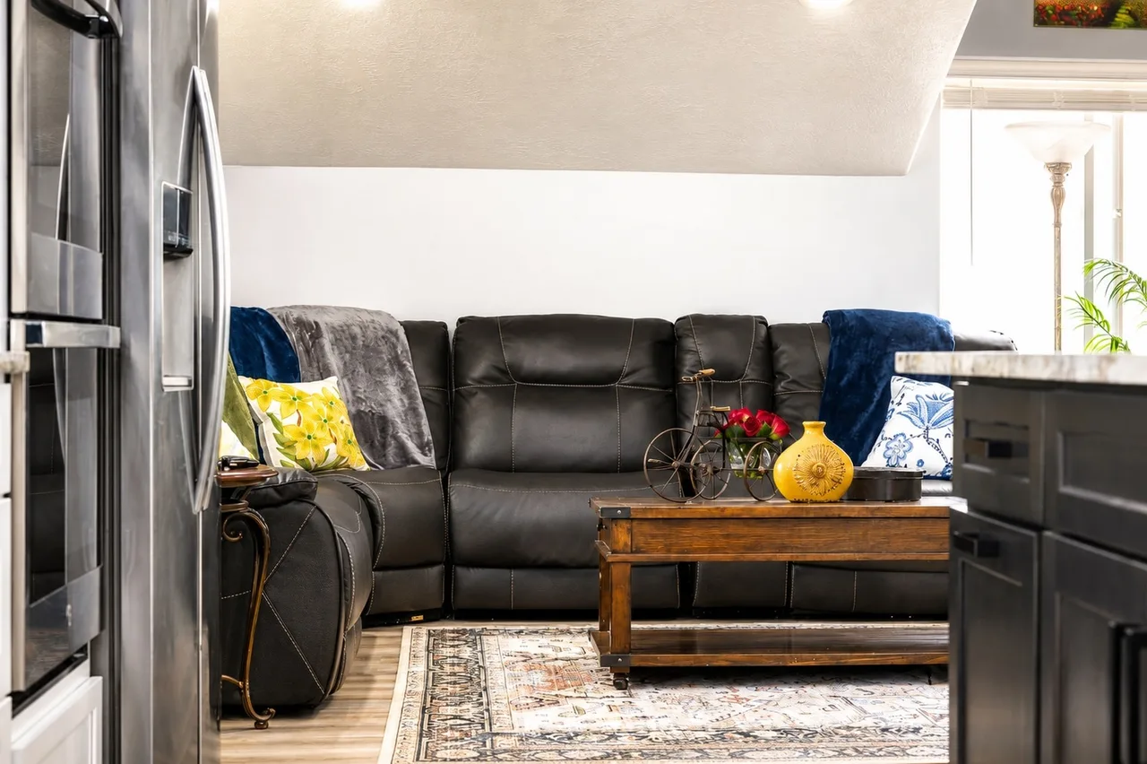 Sky Suite living area with black leather power-reclining sectional, patterned Persian rug, and a coffee-table styled with a red-flower planter.
