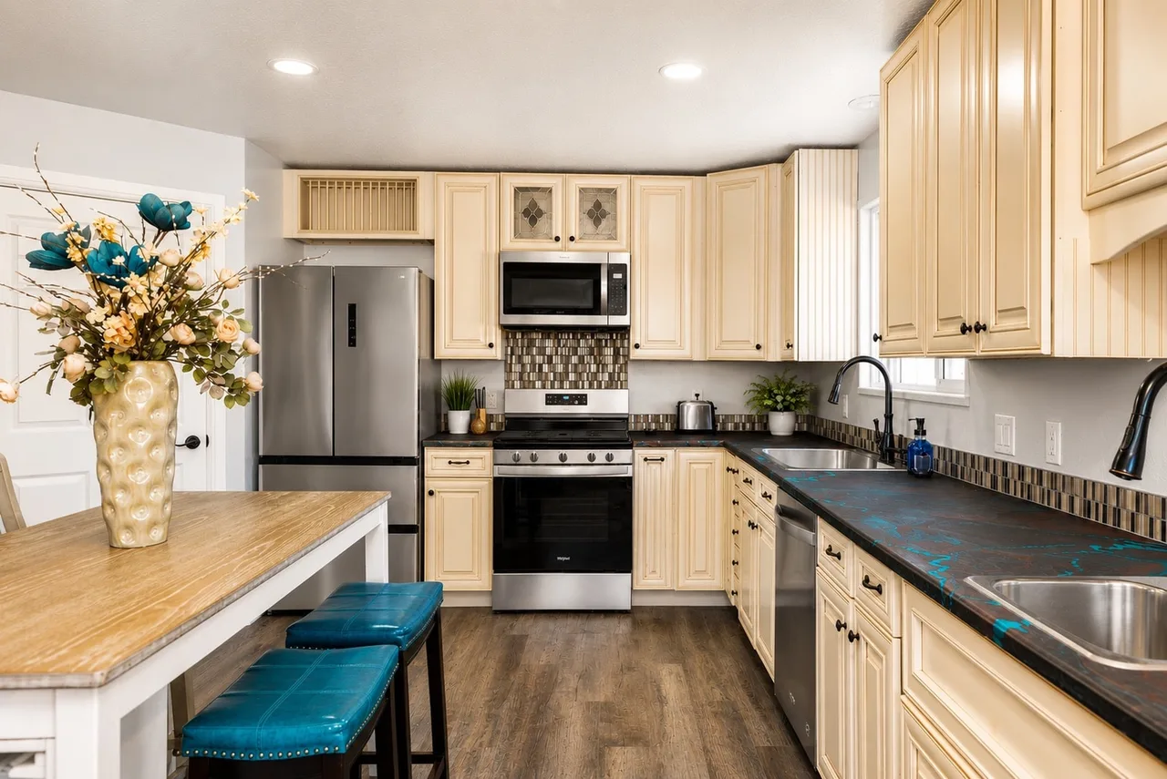 Garden Suite kitchen appliance side with stainless fridge, gas range, dishwasher, and butcher-block island seated with teal leather stools.